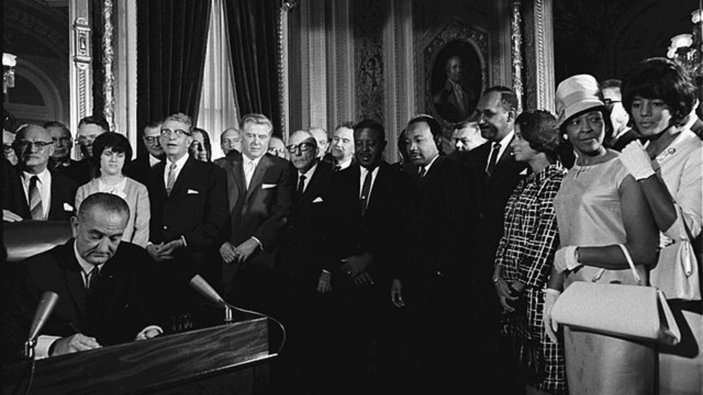 President Lyndon B. Johnson signs the Voting Rights Act of 1965 while Martin Luther King and others look on